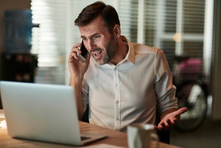 a man looking frustrated on the phone looking at his laptop.