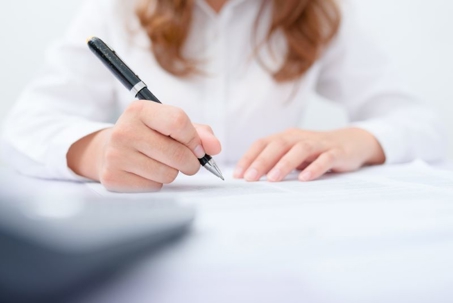 A hand in a white shirt uses a pen to write on a piece of paper.