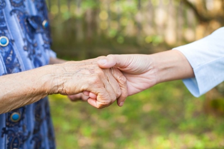 The image shows a gentle hand holding an elderly hand