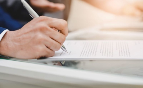 A hand in a suit signs legal documents.